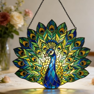 May include: A stained glass peacock with a vibrant display of blue, green, and yellow feathers. The peacock is hanging from a black chain. The glass is illuminated from behind, creating a colorful display.