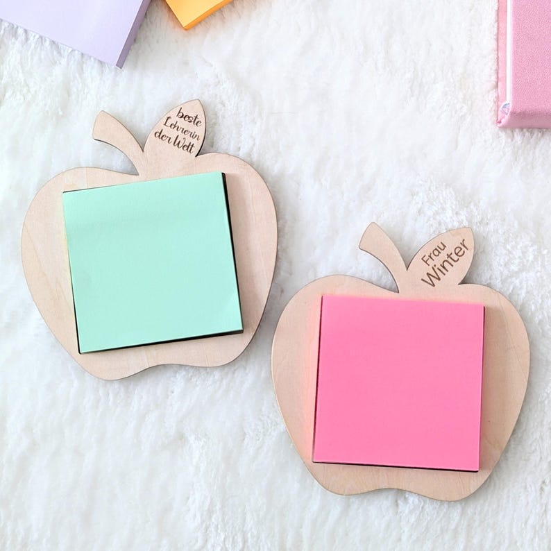 Op de afbeelding: Twee houten appelvormige memohouders met kleurrijke plaknotities. E&eacute;n heeft een lichtgroene notitie, de andere een roze notitie. Tekst op de houders luidt "beste Lehrerin der Welt" en "Frau Winter".