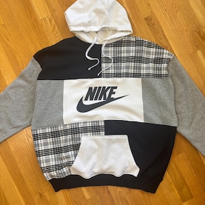 Pu&ograve; includere: Una felpa con cappuccio patchwork con cappuccio bianco e un ampio pannello bianco con il logo Nike. La felpa combina motivi neri, grigi e a quadri. Ha una tasca frontale e un cordino.