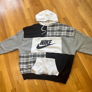 Pu&ograve; includere: Una felpa con cappuccio patchwork con cappuccio e coulisse bianchi. La felpa con cappuccio presenta pannelli grigi, neri, bianchi e a quadri. Il logo Nike &egrave; ben visibile in nero sul davanti. &Egrave; presente una tasca a marsupio.