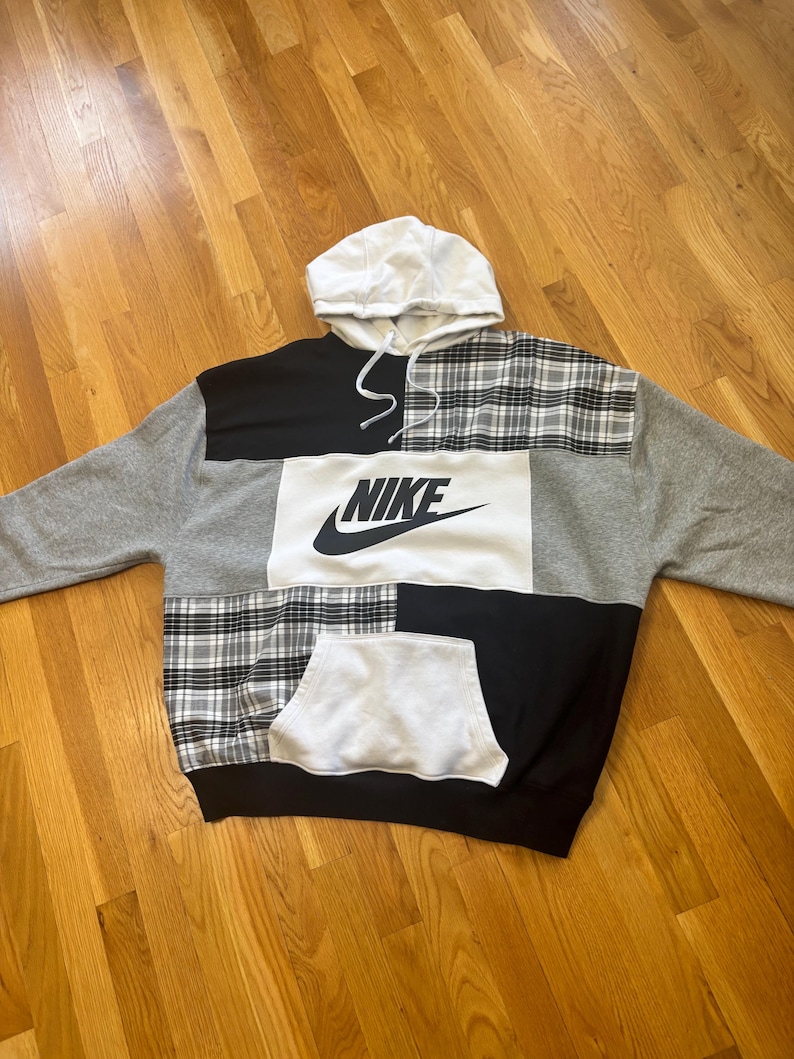 Pu&ograve; includere: Una felpa con cappuccio patchwork con cappuccio e coulisse bianchi. La felpa con cappuccio presenta pannelli grigi, neri, bianchi e a quadri. Il logo Nike &egrave; ben visibile in nero sul davanti. &Egrave; presente una tasca a marsupio.