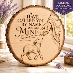 May include: A circular wooden slice featuring a laser-engraved illustration of a hand reaching toward a small lamb. The text reads: I HAVE CALLED YOU BY NAME; YOU ARE MINE, followed by ISAIAH 43:1. The wood has a natural bark edge.