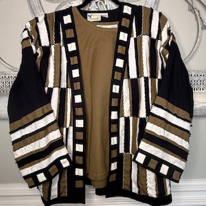 Puede incluir: Una chaqueta de manga larga abierta con un diseño de patchwork de tiras de tela negras, blancas y color canela con bordes deshilachados, sobre una camiseta color canela. La chaqueta tiene un borde a cuadros en la abertura y los puños.