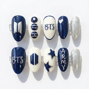 May include: A collection of ten artificial nails with diverse designs. The nails are in navy blue, white, and silver glitter. Some nails display the letters "BTS" or the word "ARMY" in silver. Other nails have silver designs.