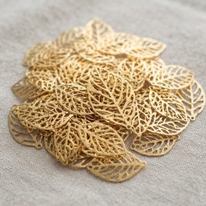 Könnte beinhalten: Eine Ansammlung von blattförmigen Anhängern aus goldfarbenem Metall mit einem komplizierten, durchbrochenen Filigranmuster. Jedes Stück ist wie ein Blatt geformt, mit sichtbaren Blattadern und einer feinen, spitzenartigen Struktur.