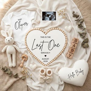 May include: A baby announcement featuring a white onesie with "Baby Oliver" printed on it, a heart-shaped sign with "This is the Last One" and "August 2026", and a "Hello Baby" pillow. Includes baby shoes, blocks, and a stuffed bunny.