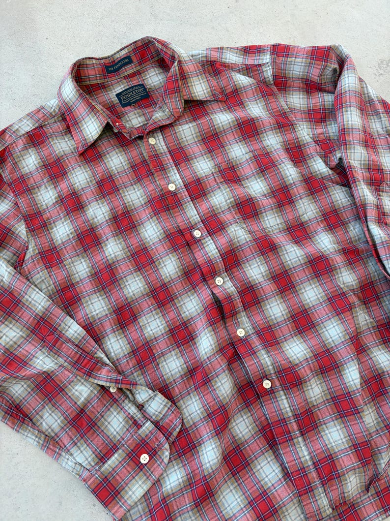 Puede incluir: Camisa abotonada a cuadros rojos, blancos y azules. La camisa tiene mangas largas y un cuello cl&aacute;sico. La etiqueta Pendleton es visible en el cuello. La camisa est&aacute; hecha de una tela suave y tejida.