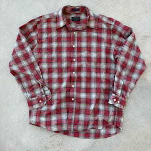 Puede incluir: Camisa a cuadros rojos y blancos con mangas largas. La camisa tiene un cuello clásico y puños abotonados. El patrón de cuadros incluye líneas azul claro y blancas. La camisa está hecha de una tela suave y tejida.