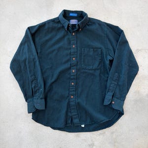 Op de afbeelding: Donkergroenblauwe button-down shirt met lange mouwen en een subtiel verticaal streepjespatroon. Voorzien van een button-down kraag, een enkele borstzak en bruine knopen. Het shirt heeft een label op de kraag.