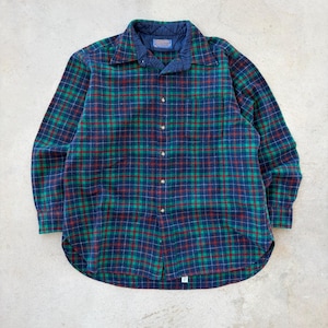 May include: A long-sleeved plaid shirt in shades of blue, green, and red. The shirt features a quilted navy blue collar and a button-down front. The fabric has a soft, textured appearance, suggesting a warm, comfortable material.
