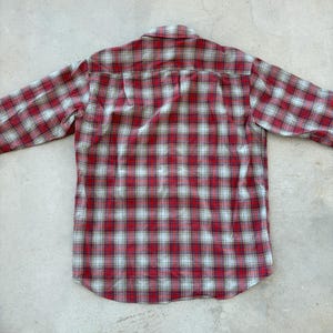 Puede incluir: Una camisa de manga larga a cuadros rojos y blancos. La camisa est&aacute; hecha de una tela suave y tejida y presenta un cuello y pu&ntilde;os abotonados cl&aacute;sicos. El patr&oacute;n de cuadros es un dise&ntilde;o tradicional, con l&iacute;neas rojas y blancas.