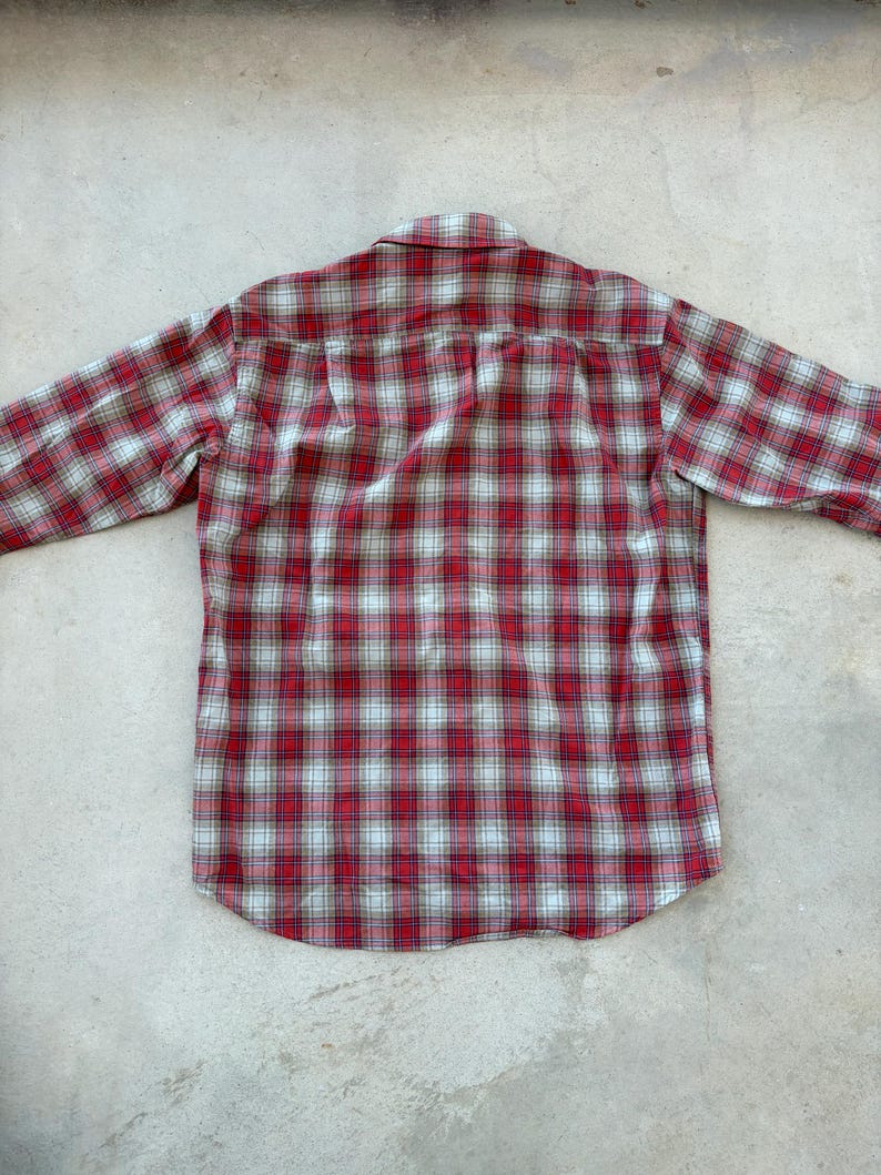 Puede incluir: Una camisa de manga larga a cuadros rojos y blancos. La camisa est&aacute; hecha de una tela suave y tejida y presenta un cuello y pu&ntilde;os abotonados cl&aacute;sicos. El patr&oacute;n de cuadros es un dise&ntilde;o tradicional, con l&iacute;neas rojas y blancas.