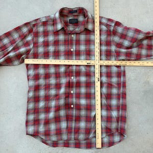 Puede incluir: Camisa a cuadros roja y gris con mangas largas. La camisa tiene un cuello cl&aacute;sico y se mide con una regla de madera. La longitud de la camisa es de aproximadamente 76 cm.