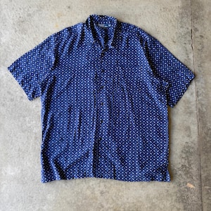 Op de afbeelding: Een overhemd met korte mouwen en knoopsluiting in een diep marineblauwe kleur met een herhalend patroon van kleine, witte, streepachtige markeringen. Het overhemd heeft een klassieke kraag, een knoopsluiting aan de voorzijde en een rechte zoom.