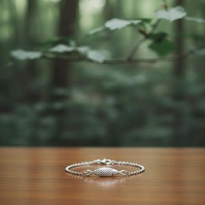 Puede incluir: Una pulsera de plata con un dije en forma de pez. La pulsera presenta una fina cadena y un diseño texturizado y punteado en el pez. La joya se exhibe sobre una superficie de madera con un fondo verde borroso.