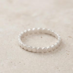 May include: A silver ring featuring a repeating dot pattern. The ring is crafted from a shiny metal and has a simple, elegant design. The dots are uniformly spaced around the band.