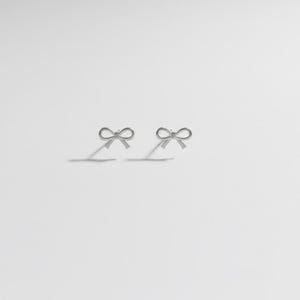 Pu&ograve; includere: Un paio di orecchini a bottone argentati a forma di fiocco. Gli orecchini sono piccoli e delicati, con un design semplice ed elegante. I fiocchi sono simmetrici e proiettano ombre sulla superficie bianca.