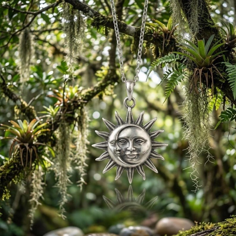May include: A silver-toned metal pendant necklace featuring a celestial design with a sun and crescent moon face. The pendant is suspended from a delicate silver chain, showcasing intricate facial features and radiating sunbeams in a metallic finish.
