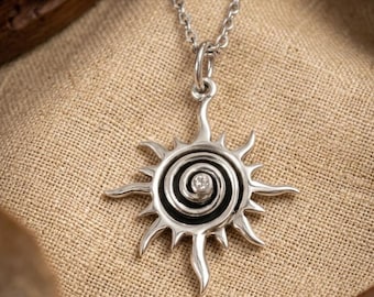 May include: A silver-toned pendant necklace featuring a sun-shaped design with a central spiral pattern and a small embedded clear stone. The pendant hangs from a delicate silver-toned chain, showcasing polished metal rays extending outward.