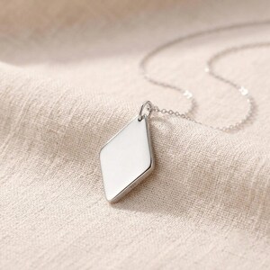 May include: A silver-toned necklace featuring a smooth, diamond-shaped pendant with a polished finish. The pendant is suspended from a delicate, thin metal chain. The metal surface of the pendant is stamped with the number 925 near the top bail.