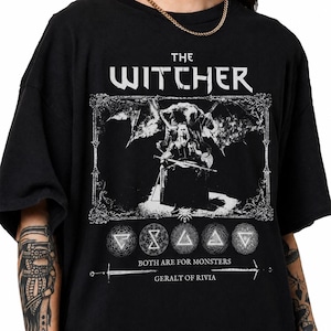 May include: A black t-shirt featuring a white graphic print of The Witcher. The design includes a central figure sitting on a throne, five circular symbols, and the text "THE WITCHER", "BOTH ARE FOR MONSTERS", and "GERALT OF RIVIA" in white.