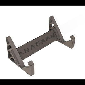 Puede incluir: Un soporte gris para teléfono con la palabra "ANAGRAM" impresa en la barra central. El soporte tiene un diseño minimalista con soportes angulados y una base rectangular. El soporte está diseñado para sostener un teléfono o tableta.