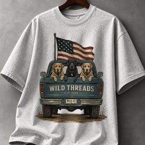 May include: A light gray t-shirt featuring a graphic of three dogs in a blue pickup truck with an American flag. The truck has the words "WILD THREADS - EST. 2024" printed on the back.