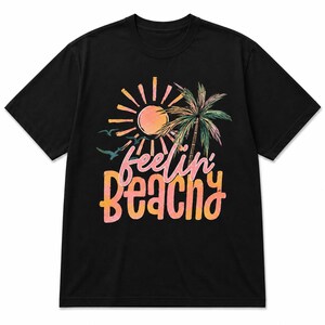May include: Black t-shirt featuring a colorful beach-themed graphic. The design includes a sun, palm tree, and the words "feelin' beachy" in a playful font. The shirt is made of a soft material.