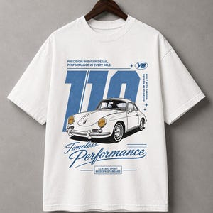 Puede incluir: Camiseta blanca con un gráfico de coche retro en blanco y azul. El diseño incluye el número "110" y las palabras "Timeless Performance" y "Classic Spirit Modern Standard". La camiseta tiene cuello redondo y mangas cortas.