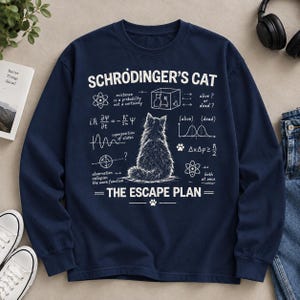 May include: A navy blue long-sleeve sweatshirt featuring a white graphic of a cat sitting with its back to the viewer. The design includes the text "SCHRODINGER'S CAT" and "THE ESCAPE PLAN" alongside various physics equations, diagrams, and paw prints.