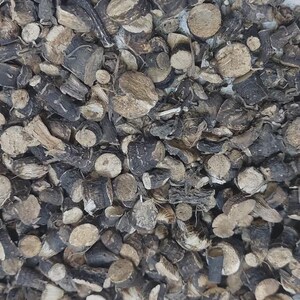 May include: A collection of small, dried, cylindrical plant root pieces. Each piece features a dark brown to black outer bark and a light beige, fibrous interior. The fragments vary in size and shape, creating a dense, textured pile of organic material.