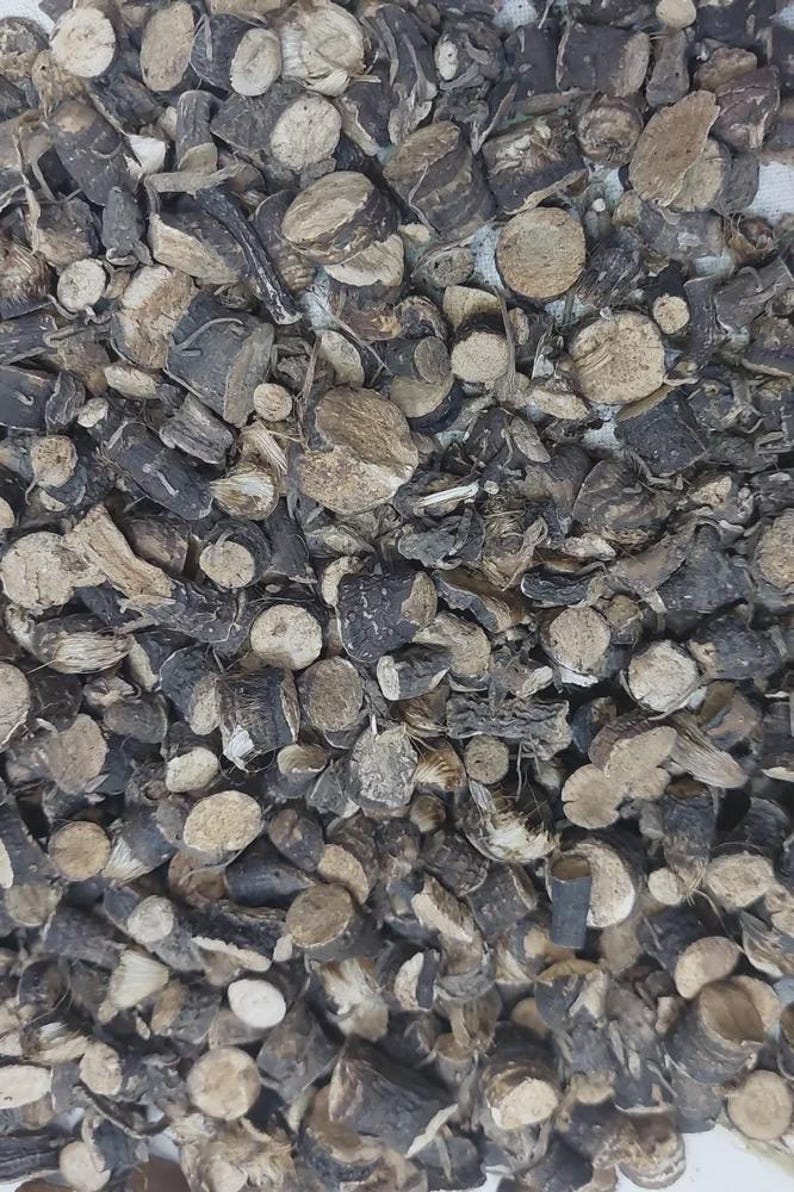 May include: A collection of small, dried, cylindrical plant root pieces. Each piece features a dark brown to black outer bark and a light beige, fibrous interior. The fragments vary in size and shape, creating a dense, textured pile of organic material.