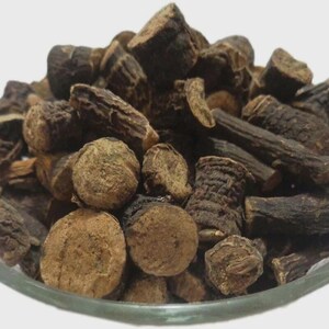 May include: A clear glass bowl filled with dried, dark brown pieces of a plant. The pieces vary in shape, including round, cylindrical, and irregular forms. The plant matter has a rough, textured appearance.