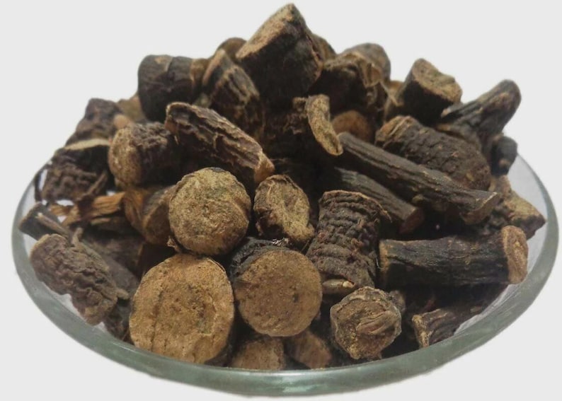 May include: A clear glass bowl filled with dried, dark brown pieces of a plant. The pieces vary in shape, including round, cylindrical, and irregular forms. The plant matter has a rough, textured appearance.