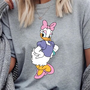 Puede incluir: Sudadera gris con un gr&aacute;fico de Daisy Duck. El personaje de dibujos animados lleva un lazo rosa, una blusa morada y zapatos amarillos y rosas. La sudadera es de estilo casual.