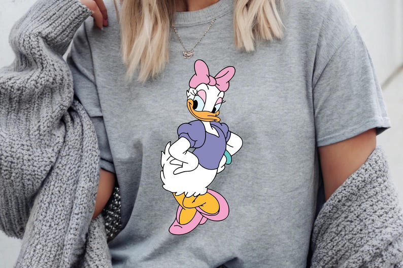 Puede incluir: Sudadera gris con un gr&aacute;fico de Daisy Duck. El personaje de dibujos animados lleva un lazo rosa, una blusa morada y zapatos amarillos y rosas. La sudadera es de estilo casual.
