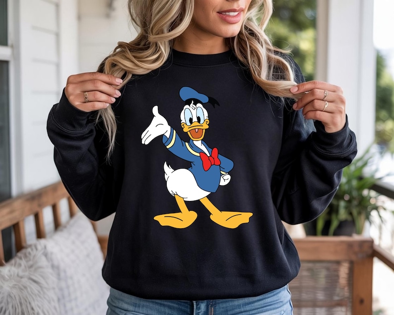 Puede incluir: Sudadera negra con un gr&aacute;fico colorido de Donald Duck con un atuendo de marinero. El personaje de dibujos animados lleva un traje de marinero azul, una pajarita roja y un gorro de marinero. La sudadera es de cuello redondo.