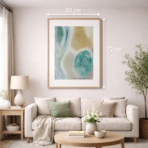 Puede incluir: Una impresión artística abstracta enmarcada, de 52 cm de ancho y 72 cm de alto, cuelga sobre un sofá. La obra de arte presenta una mezcla de tonos azules, verdes y beige. La habitación está decorada con una paleta de colores neutros.