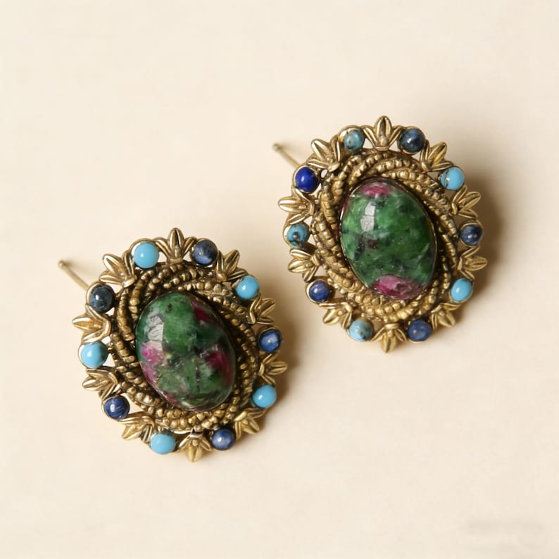 Peut inclure: Une paire de boucles d'oreilles &agrave; clous de style vintage. Chaque boucle d'oreille pr&eacute;sente une pierre ovale verte et rouge, entour&eacute;e de petites pierres bleues et turquoise, sertie dans un cadre en m&eacute;tal dor&eacute;.