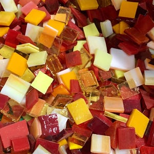 May include: A collection of small, square glass tiles in shades of red, orange, and yellow. The tiles are perfect for mosaic projects.