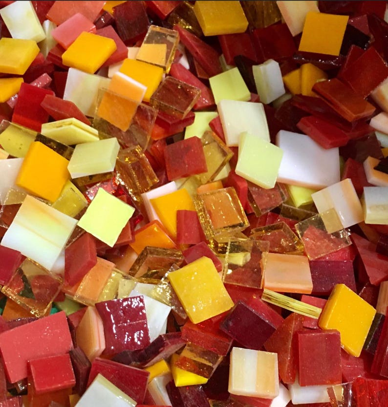 May include: A collection of small, square glass tiles in shades of red, orange, and yellow. The tiles are perfect for mosaic projects.