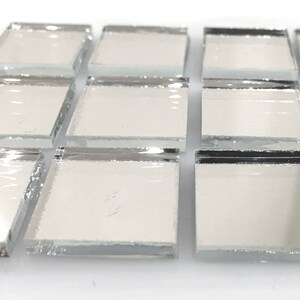 May include: A close-up of a sheet of small, square, silver-backed mirror tiles. The tiles are arranged in rows and columns, and the edges of the tiles are visible.