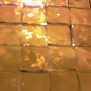 May include: A close-up of a gold mosaic tile wall. The tiles are arranged in a grid pattern and have a reflective surface.