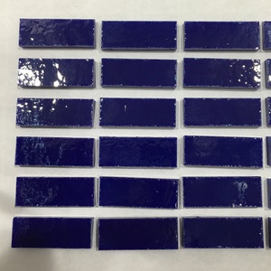 May include: A collection of rectangular tiles arranged in a grid pattern. Each tile features a deep, glossy royal blue finish with a smooth, reflective surface. The tiles are uniform in shape and size, displaying a consistent dark blue color.