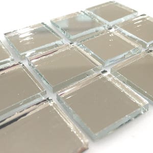 May include: Silver mirrored glass tiles arranged in a staggered pattern. The tiles are square and have a reflective surface.