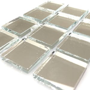 May include: A collection of small, square, silver-toned mirror tiles. The tiles have a slightly irregular, chipped edge, giving them a rustic look.