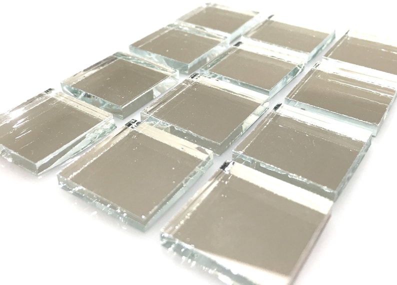 May include: A collection of small, square, silver-toned mirror tiles. The tiles have a slightly irregular, chipped edge, giving them a rustic look.