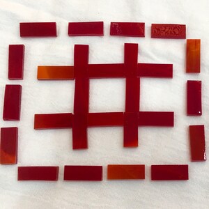 May include: A collection of rectangular red glass tiles arranged in a grid pattern. The tiles are laid out to form a central hashtag shape surrounded by a rectangular border of individual tiles, all featuring a smooth, glossy finish.