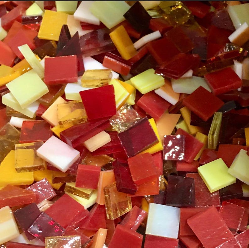 May include: A close-up of a variety of small, square glass tiles in shades of red, orange, yellow, and white. The tiles are perfect for mosaic projects and crafts.