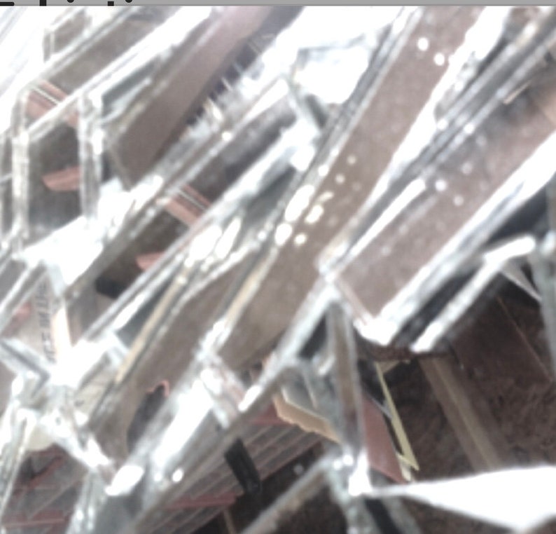 May include: A close-up of a broken window pane with shards of glass reflecting light. The glass is shattered and creates a pattern of lines and angles.
